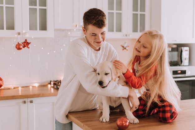 Los niños con su amado perro están sentados en la cocina navideña. pasatiempo familiar. estilo de vida. hermano y hermana, niño y niña juegan y juegan con una mascota. espacio para texto. foto de alta calidad