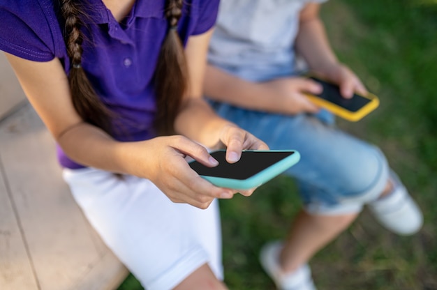 Niños con teléfonos inteligentes al aire libre en verano.