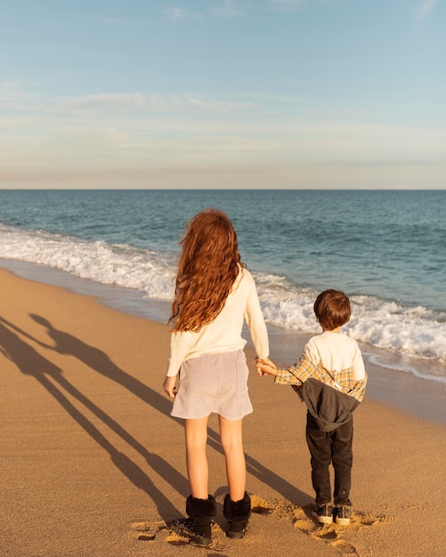 Foto niños de tiro completo tomados de la mano en la playa