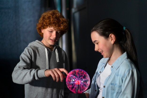 Niños de tiro medio interactuando con una bola de plasma