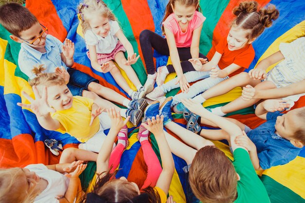 Foto niños tomados de la mano juntos sentados en paracaídas arco iris, concepto de trabajo en equipo de niños