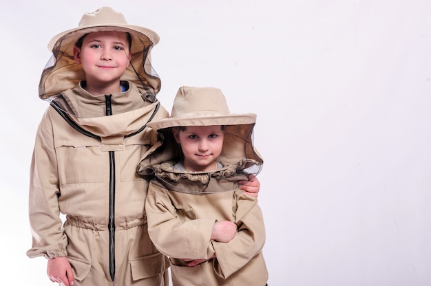 Niños en trajes de apicultor posando en fondo blanco de estudio.