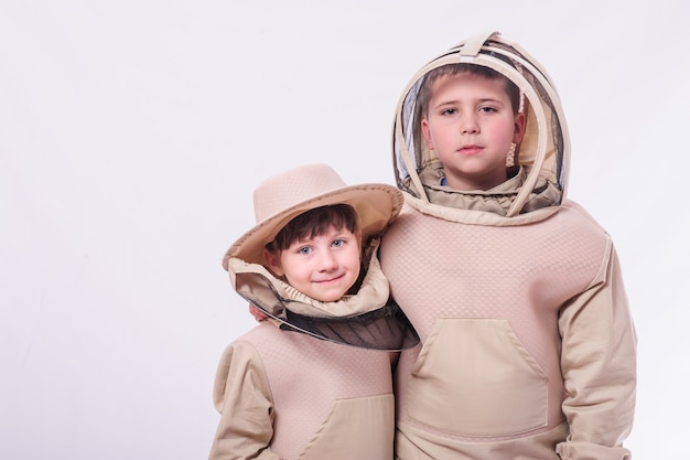 Niños en trajes de apicultor posando en fondo blanco de estudio.