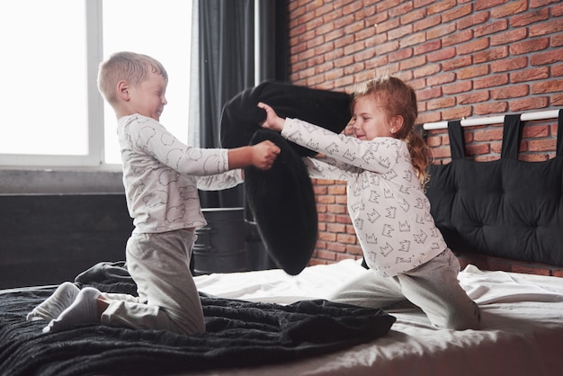 Niños traviesos El niño y la niña organizaron una pelea de almohadas en la cama de la habitación. Les gusta ese tipo de juego