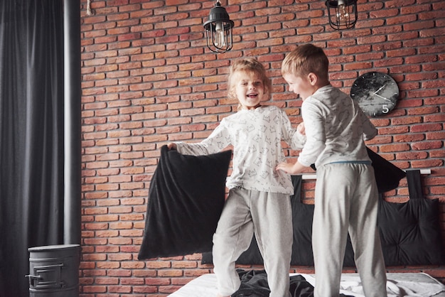 Niños traviesos El niño y la niña organizaron una pelea de almohadas en la cama de la habitación. Les gusta ese tipo de juego