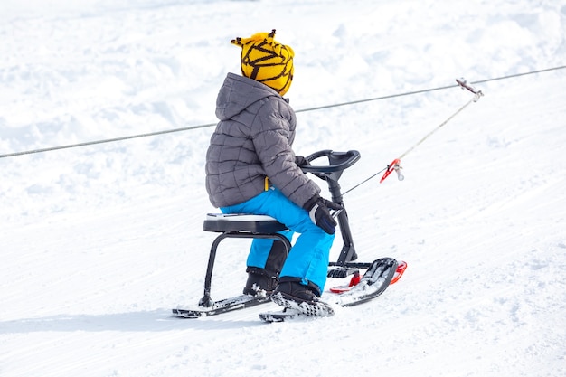 Niños con trineo de escalada en la colina nevada en Winter Park en Bakuriani