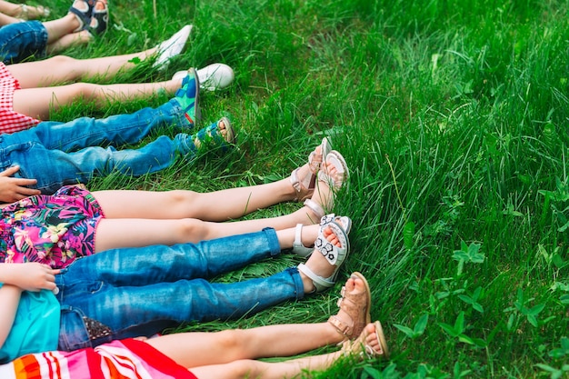 Niños tumbados en la hierba verde en el parque en un día de verano con las piernas levantadas hacia el cielo.