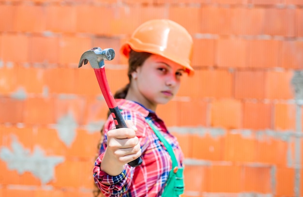 Los niños usan casco en el sitio de construcción. jovencita constructora con herramienta de construcción martillo. niño en trabajos de reparación. concepto de renovación en taller. carpintero profesional ocupado. Reparar.