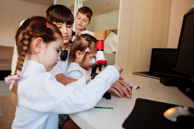 Niños usando microscopio aprendiendo clases de ciencia en casa.