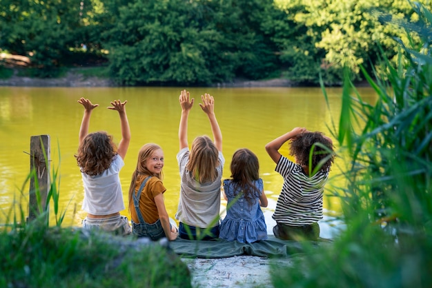 Foto niños de vista trasera sentados junto al lago