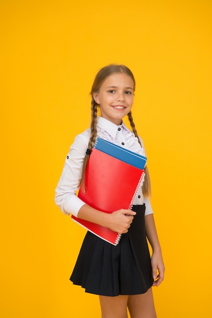 Nivel básico Colegiala feliz sostiene libros de texto fondo amarillo Colegiala de regreso a la escuela Colegiala pequeña usa uniforme Colegiala linda Educación escolar Cursos para niños superdotados