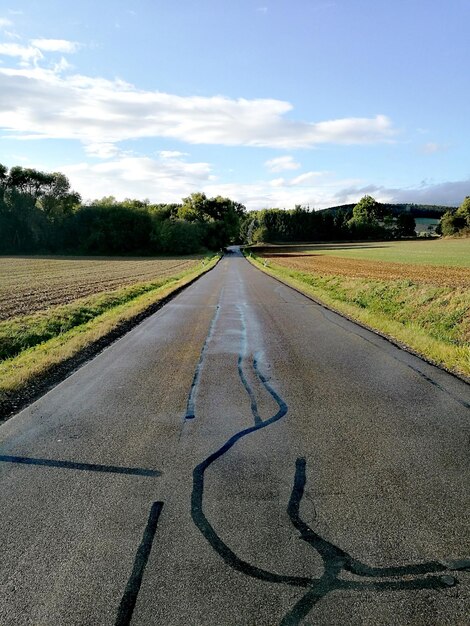 Nível de superfície de uma estrada vazia em meio a um campo contra o céu