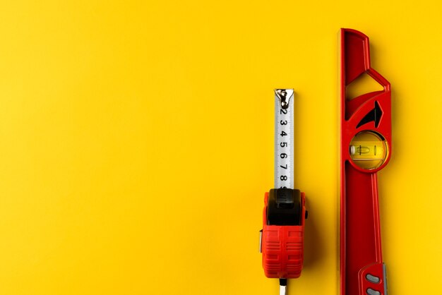 Nivel del edificio rojo y cinta métrica sobre fondo amarillo.