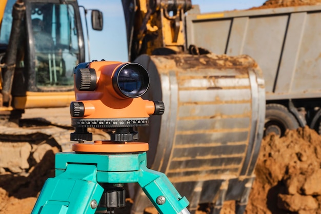 Nivel con una excavadora al fondo Nivel de construcción o teodolito Instrumentos y equipos geodésicos para la construcción y movimiento de tierras