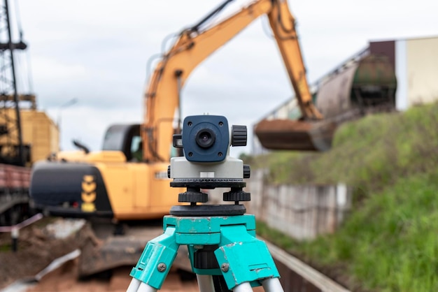 Nivel con una excavadora al fondo Nivel de construcción o teodolito Instrumentos y equipos geodésicos para la construcción y movimiento de tierras