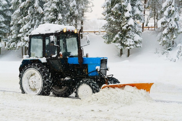 El nivelador de quitanieves azul despeja la carretera de la estación de esquí cubierta de nieve en las montañas o en la calle de la ciudad Copo de nieve de invierno nevada niebla fría niebla clima Espacio de copia horizontal