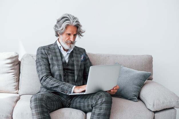 No apartamento com roupas elegantes Homem moderno elegante sênior com cabelos grisalhos e barba dentro de casa