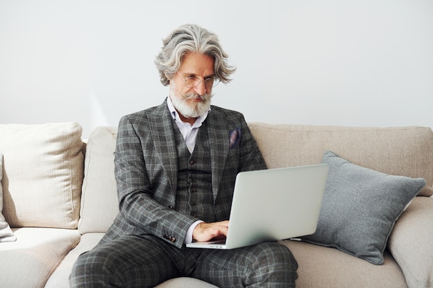 No apartamento com roupas elegantes Homem moderno elegante sênior com cabelos grisalhos e barba dentro de casa