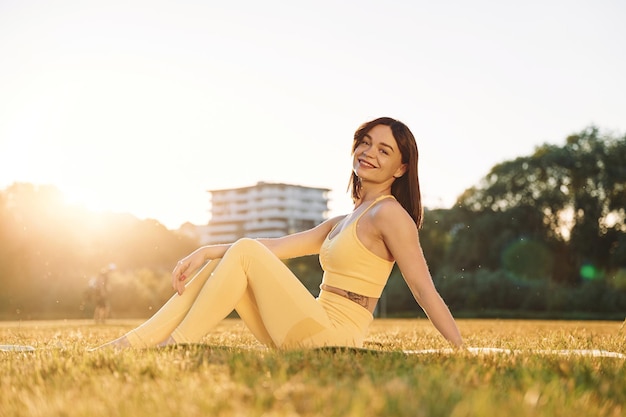 No chão Mulher bonita em roupas esportivas fazendo exercícios de fitness ao ar livre no campo