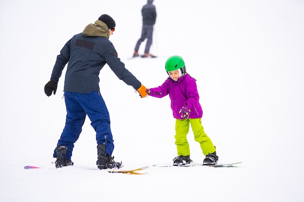 No Cold Winder Day na estação de esqui de montanha, o pai ensinando a filha pequena a fazer snowboard