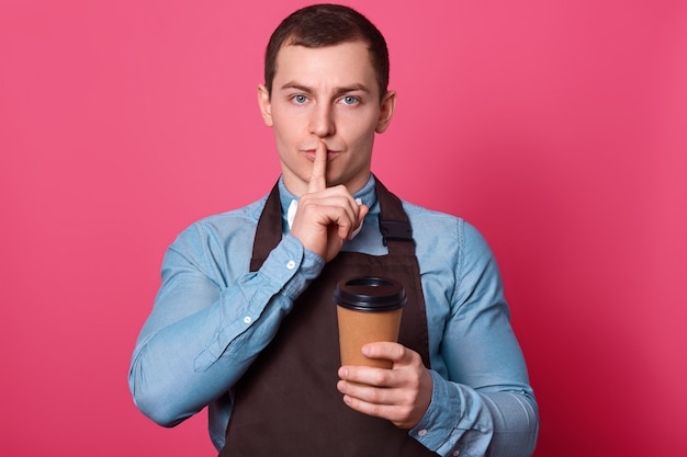 No cuentes el secreto de hacer café. El misterioso y guapo barista masculino trabaja en la cafetería, hace un gesto de silencio, mantiene el dedo índice sobre la boca