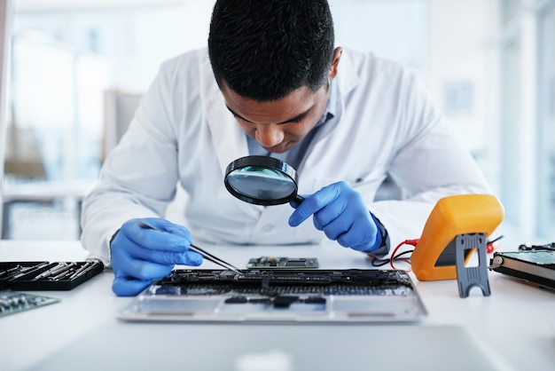 No deje ningún chip sin remover Foto de un joven que usa pinzas y una lupa mientras repara el hardware de una computadora en un laboratorio