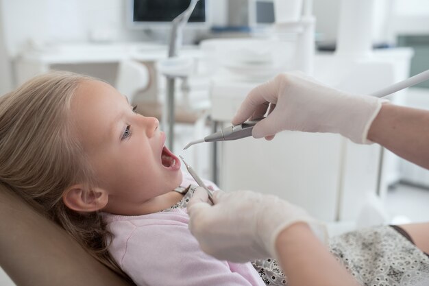 No dentista. Menininha sentada com a boca aberta no dentista