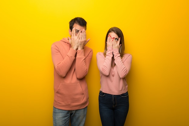 No dia dos namorados Grupo de duas pessoas em fundo amarelo cobrindo os olhos pelas mãos e olhando através dos dedos