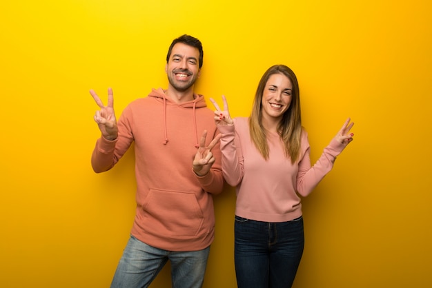 No dia dos namorados grupo de duas pessoas no fundo amarelo sorrindo e mostrando sinal de vitória com as duas mãos