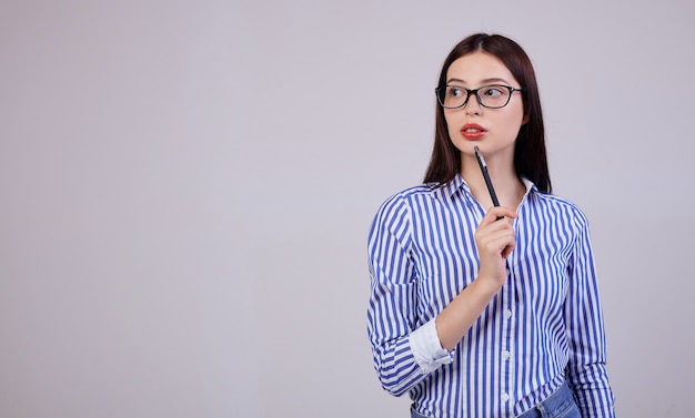 No é uma agradável jovem mulher de negócios com cabelos escuros e óculos de computador. mulher tem uma caneta preta na mão. olhando pensativamente para o lado