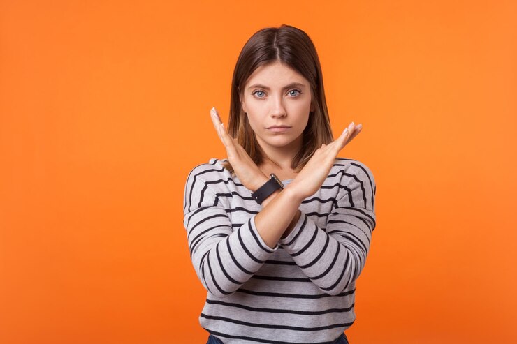 Foto no hay forma. retrato de una mujer seria y resuelta con cabello castaño en camisa a rayas de manga larga de pie con los brazos cruzados y sin gestos. tiro de estudio interior aislado sobre fondo naranja