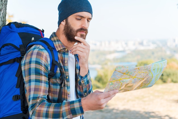 No hay este lugar en el mapa. Hombre joven pensativo con mochila y mirando a través de un mapa