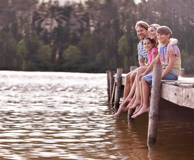 No hay nada mejor que las vacaciones familiares anuales en el lago Una familia feliz de cuatro personas sentada en un embarcadero en el lago