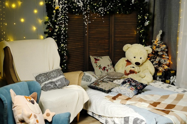 No interior da sala de Natal há uma cama grande com brinquedos macios e travesseiros ao lado da cama há uma poltrona Zona de fotos de Ano Novo Infantil