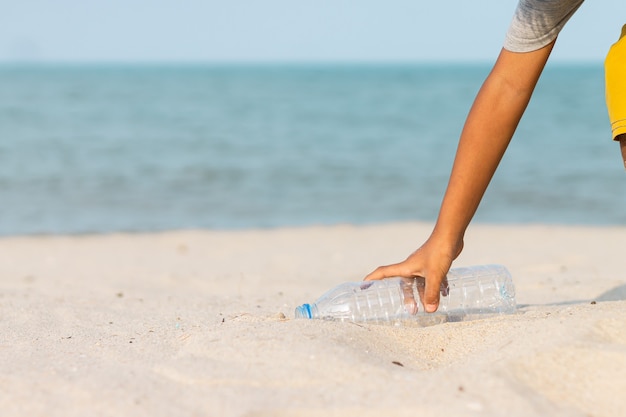 No mar, um garotinho pegando uma garrafa de plástico na praia para jogar no lixo.