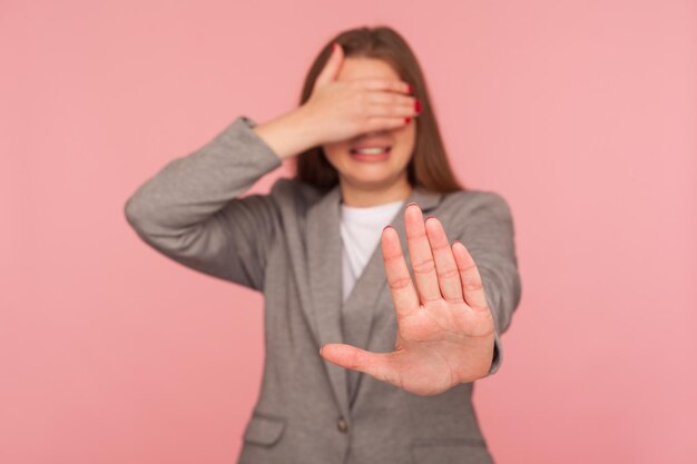 No me muestres. Retrato de una joven disgustada con traje de negocios que cubre los ojos y se detiene gesticulando, su rostro expresa disgusto y vergüenza, negándose a mirar. tiro de estudio interior, aislado