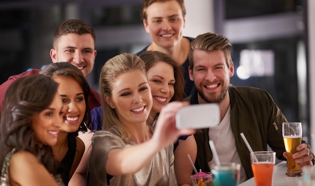 No necesitamos una excusa para una selfie Foto de un grupo de amigos felices tomándose una selfie mientras toman una copa en un bar juntos