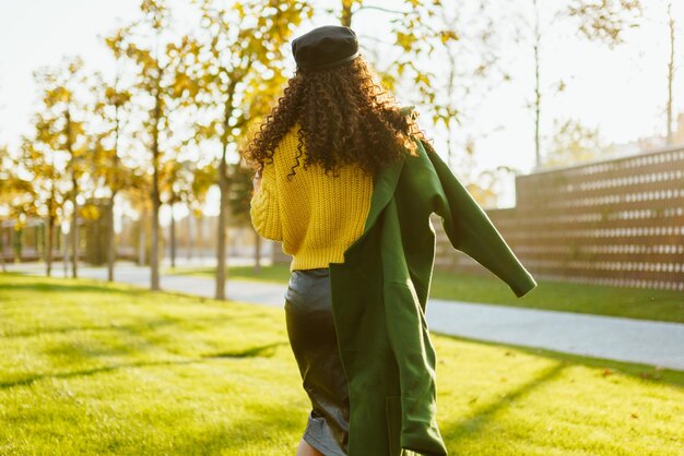 No parque, a grama é removida da câmera garota com cabelos longos e cacheados em um boné com um casaco jogado sobre um ombro