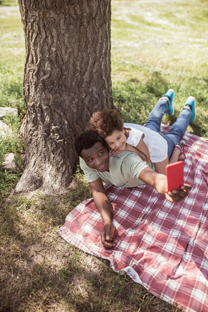 Foto no parque. homem de pele escura fazendo selfie com sua filha no parque