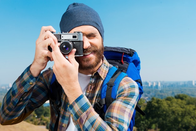 No se puede perder un paisaje tan hermoso. Apuesto joven llevando mochila y tomando una foto de una vista