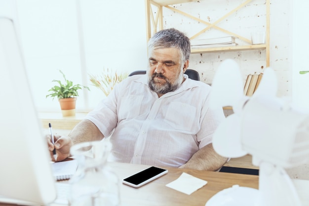 No puedo concentrarme. Hombre de negocios, gerente en la oficina con computadora y ventilador enfriándose, sensación de calor. Utilizando ventilador pero aún sufriendo un clima incómodo en el gabinete. Verano, trabajo de oficina, negocios.