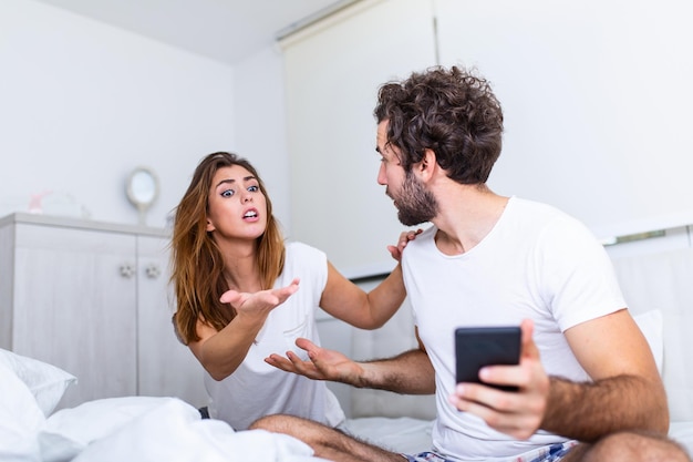 Foto no puedo soportar cuando está trabajando todo el tiempo. joven infeliz y su novio que usa el teléfono en la cama. conflicto familiar con el esposo de la esposa en la cama