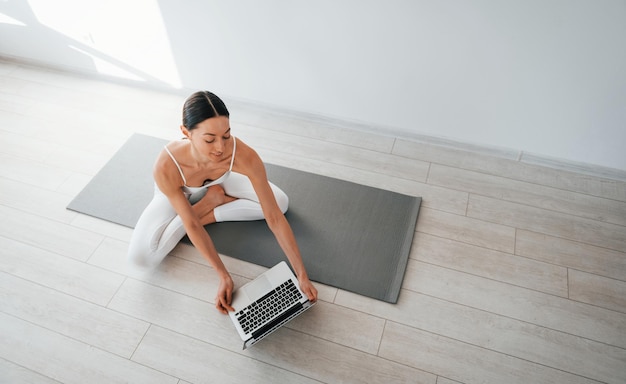 No tapete de ioga Jovem mulher caucasiana com corpo esbelto está dentro de casa durante o dia