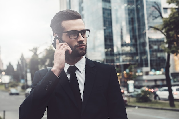 No telefone. Jovem confiante de terno falando ao celular