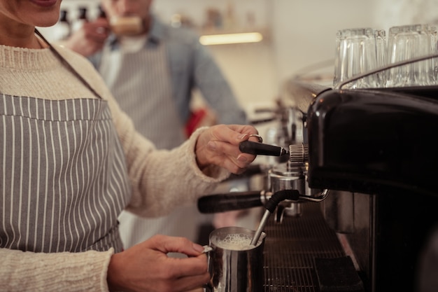 No trabalho. lindas mãos de barista fumegando leite na jarra para uma xícara de café.