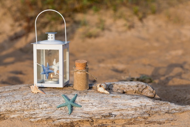 No velho log em uma lanterna de estilo náutico, conchas, uma garrafa de areia e uma estrela do mar na areia