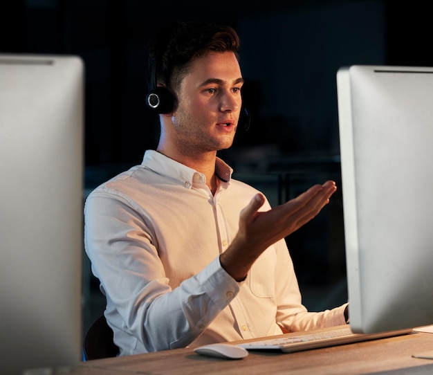 Noche de centro de llamadas y hombre que usa computadora durante la consulta para ventas de telemercadeo y atención al cliente en una oficina oscura de CRM Hombre hablando en línea para telecomunicaciones contáctenos y ayude con preguntas frecuentes