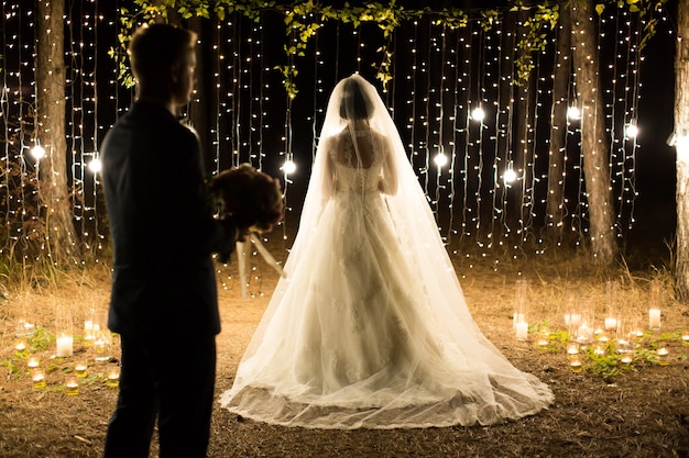 Noche de ceremonia de boda. Encuentro de los recién casados, los novios en el pinar de coníferas de velas y bombillas.