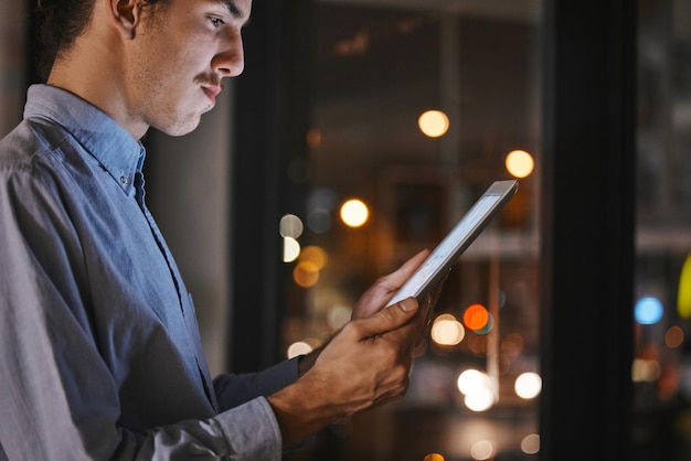 Noche de empresario y oficina con tableta en las manos para investigación, análisis de mercado y comunicación en el trabajo Man mobile touchscreen ux y lectura para análisis de datos, progreso y crecimiento de la empresa