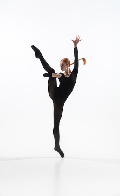Noche. Joven y elegante bailarina de ballet en estilo minimalista negro aislado sobre fondo blanco de estudio. Arte, movimiento, acción, flexibilidad, concepto de inspiración. Bailarina de ballet caucásica flexible.